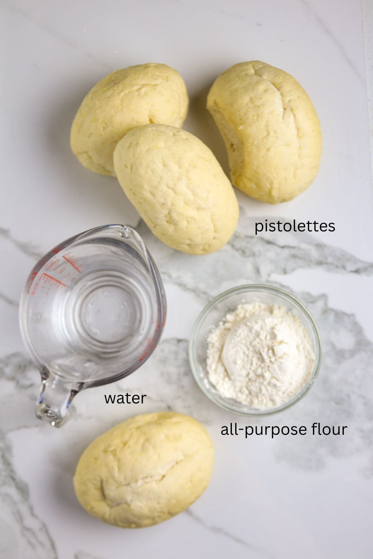 Four small bread rolls with a cup of water and a small bowl of flour.