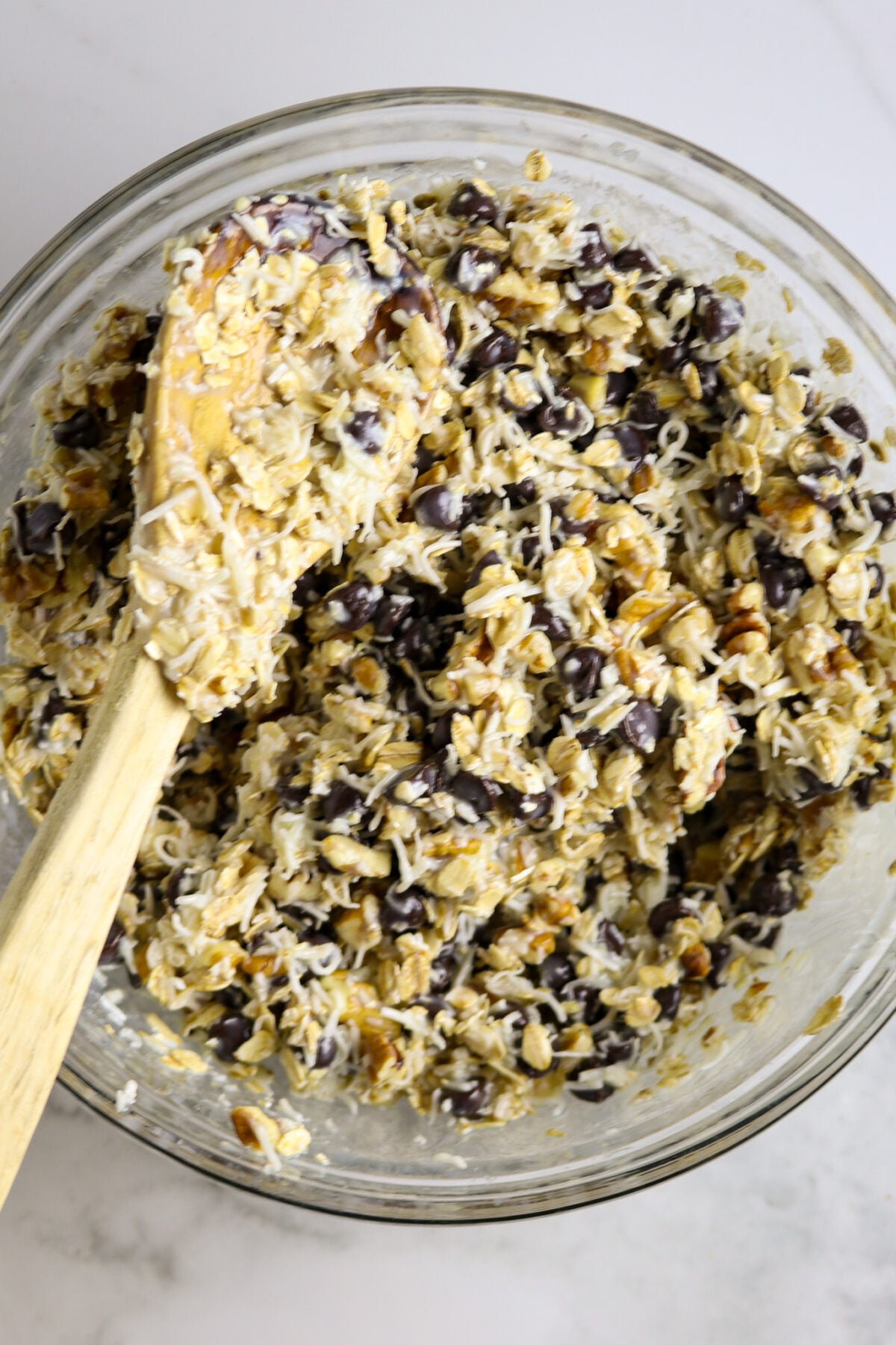 A glass bowl of mixed cookie ingredients with a wooden spoon resting on top.