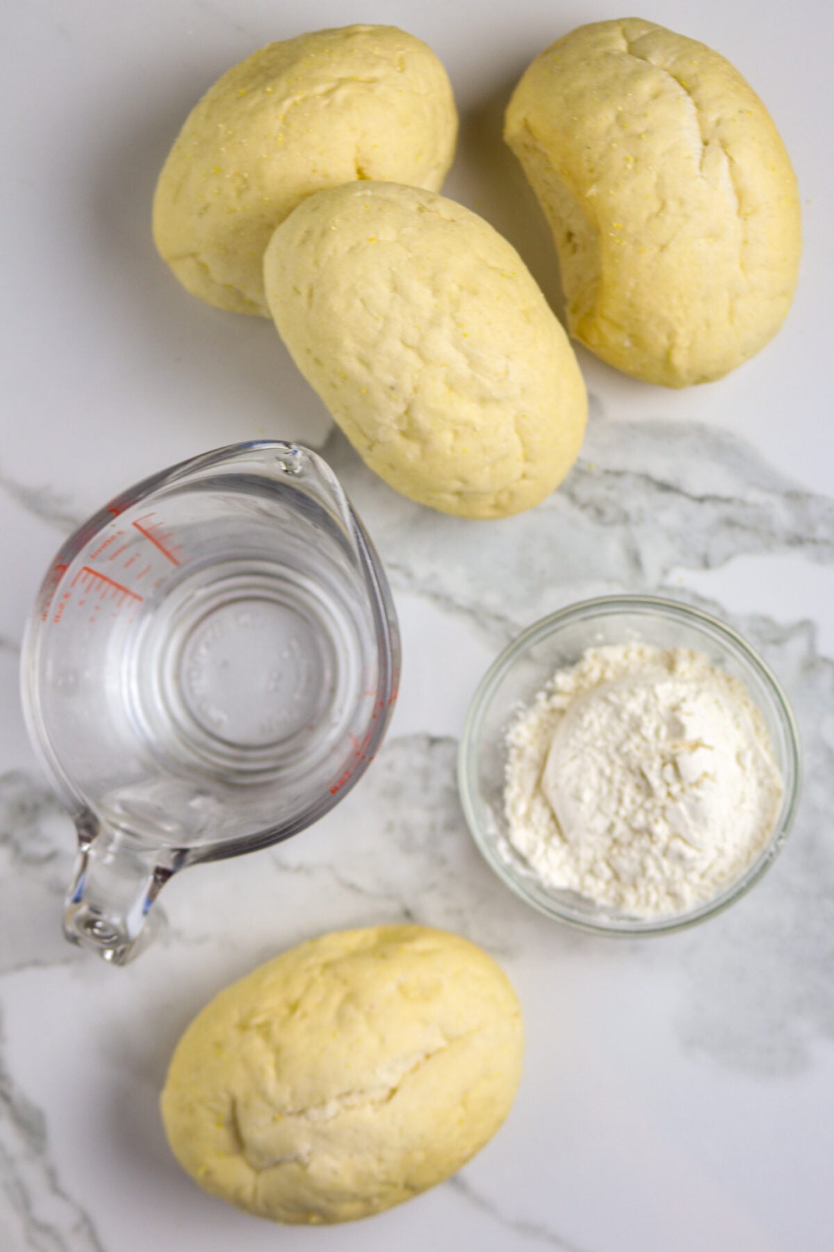 A glass measuring cup of water, a bowl of flour, and 4 small pistolette rolls for shrimp pistolettes.