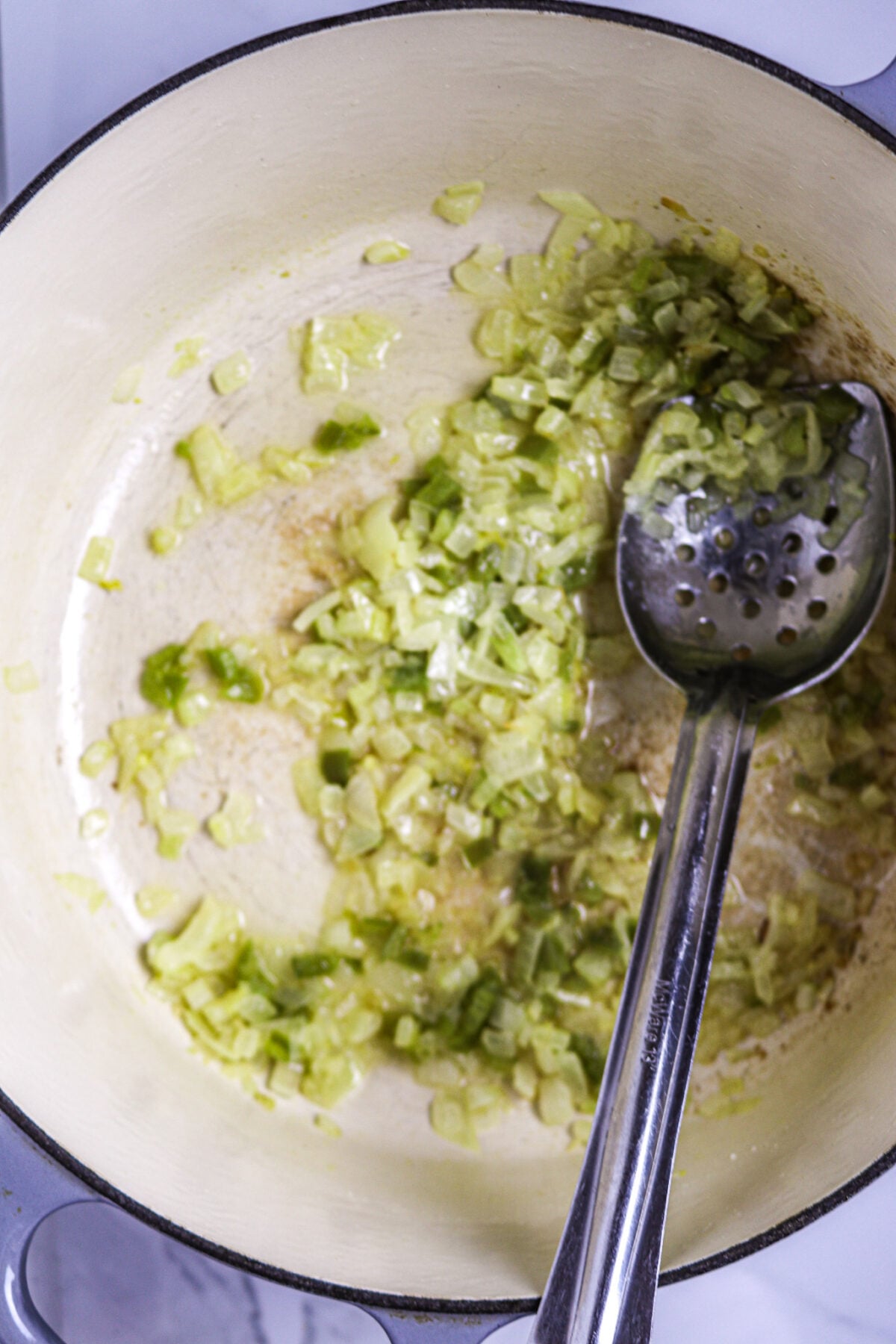 Chopped onion, celery, and green onion in melted butter with a long-handled silver spoon in a white pot for shrimp pistolettes.