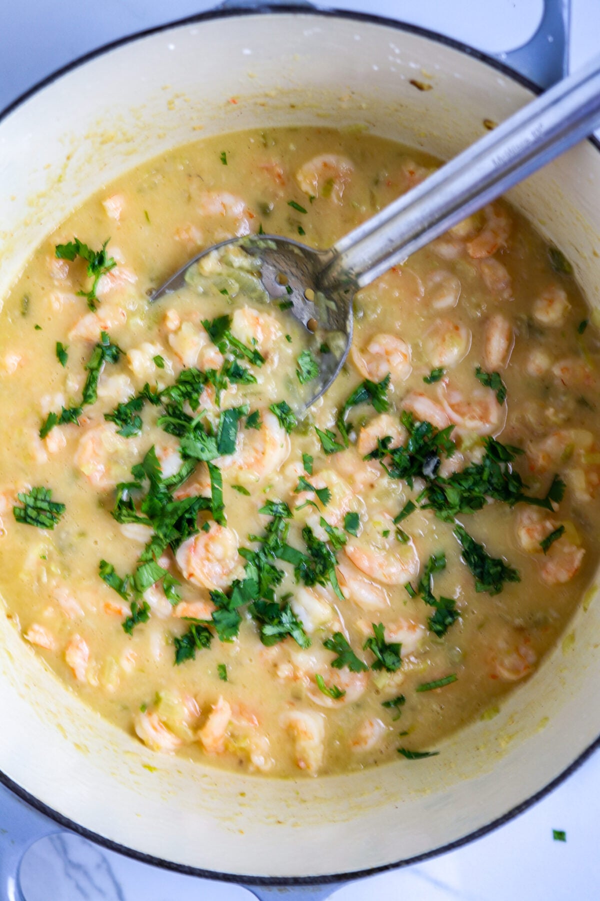 A silver spoon stirring shrimp in a creamy sauce for shrimp pistolettes with chopped parsley sprinkled on top.