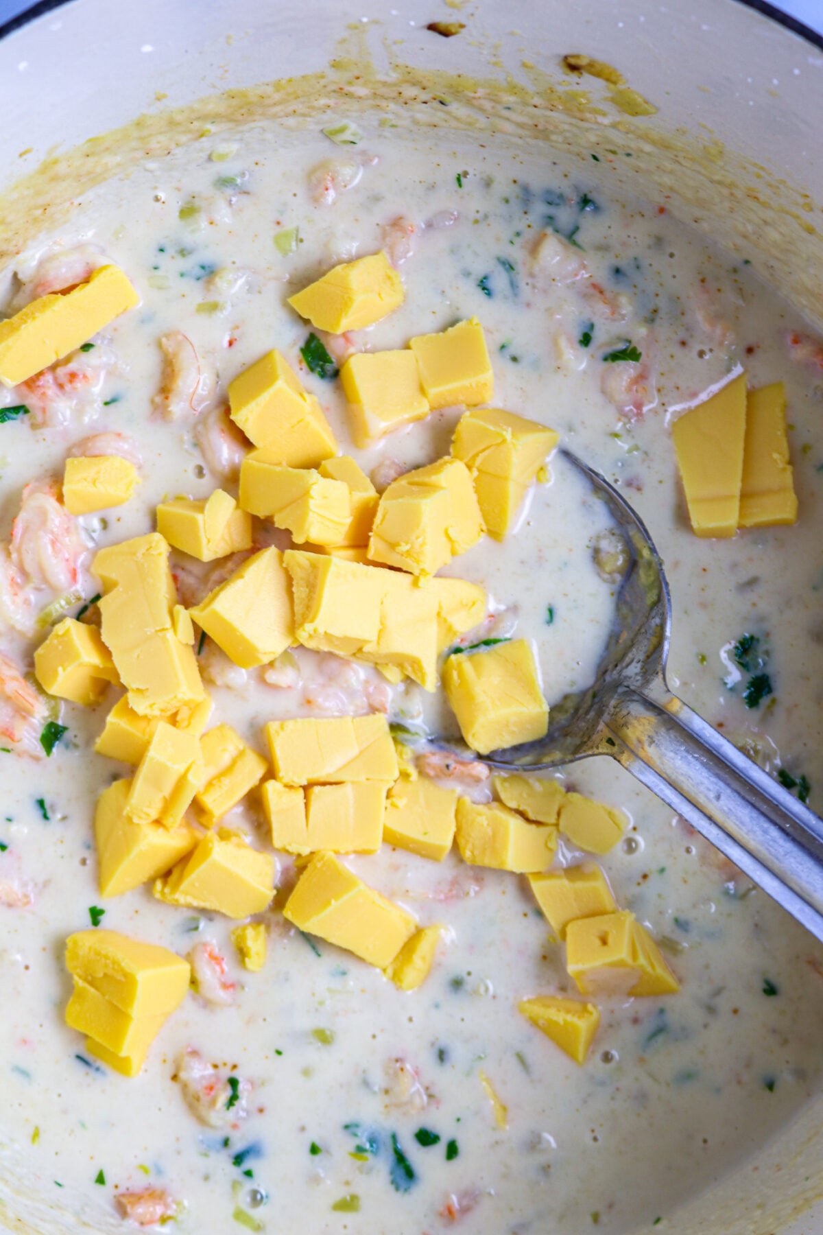 Cubes of yellow cheese in a white sauce with a silver spoon in it.