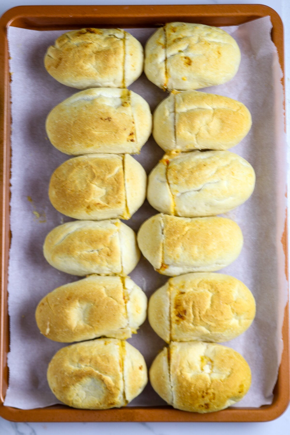 Twelve browned rolls on a parchment-lined copper cookie sheet.