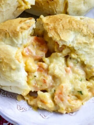 A shrimp pistolette on a plate cut in two with sauce coming out of the roll.