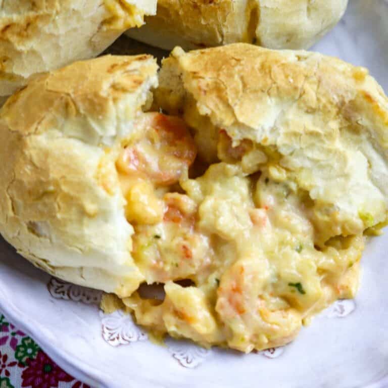 A shrimp pistolette on a plate cut in two with sauce coming out of the roll.