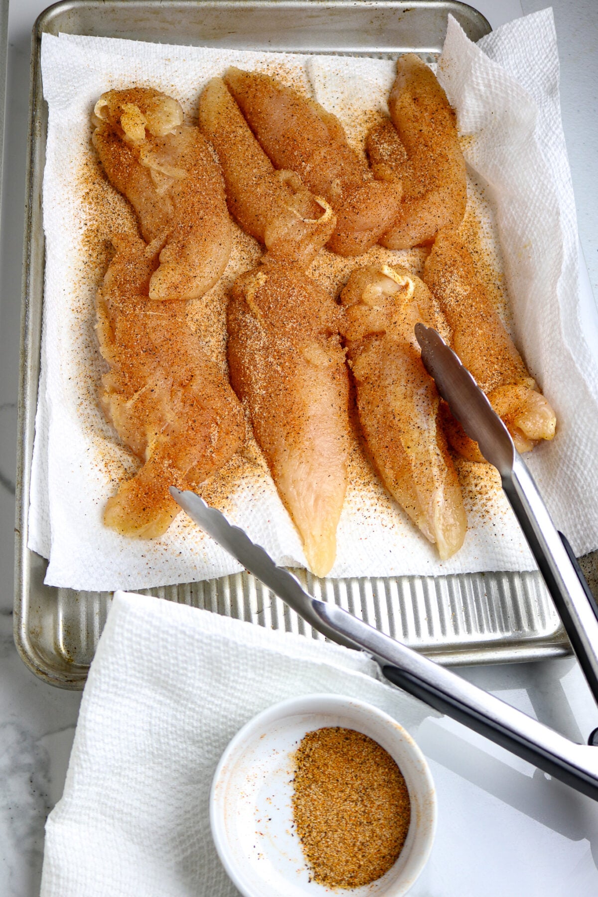 A pan of seasoned chicken tenders on a paper towel.