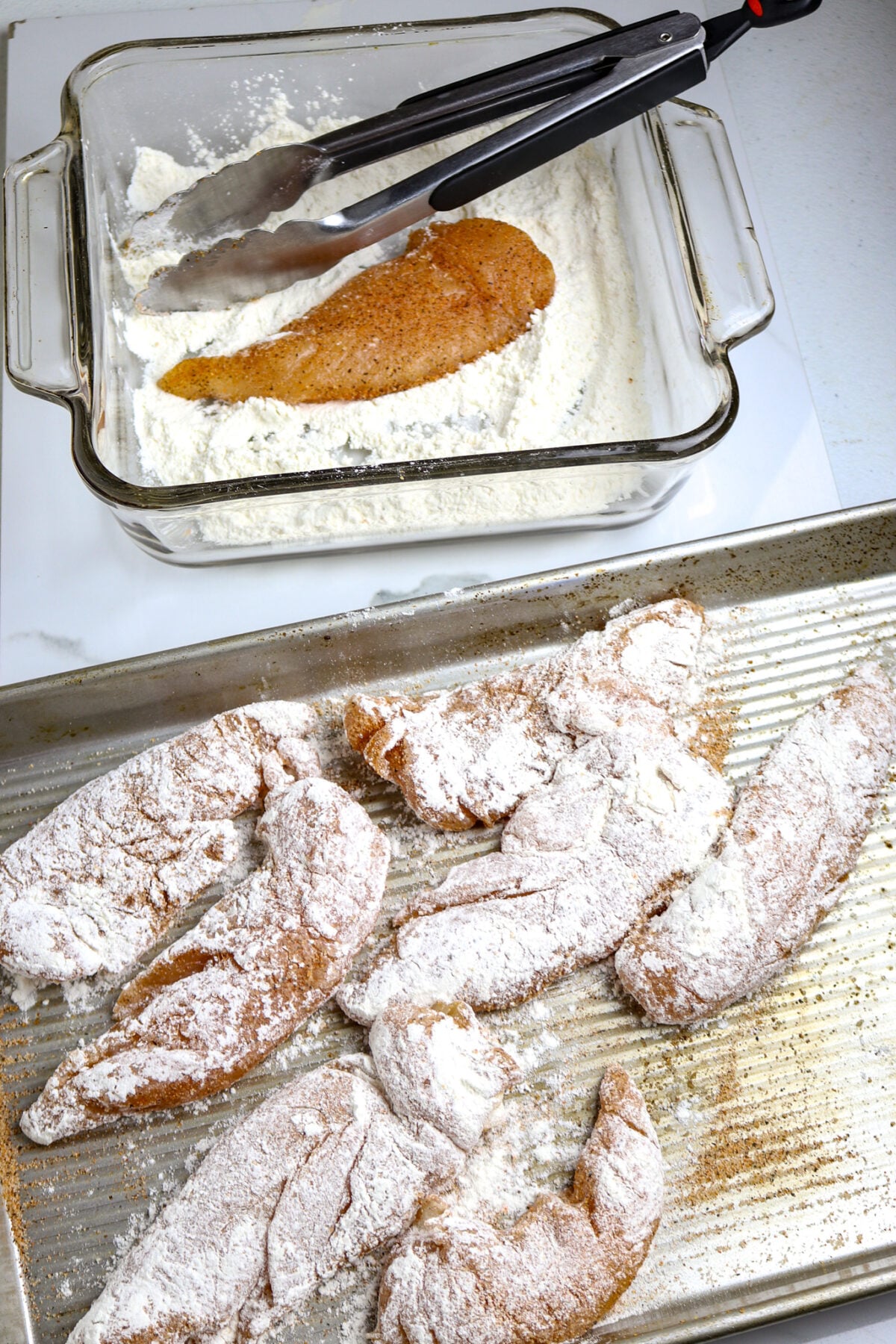 A pan of floured chicken tenders and a dish of flour with a chicken tender laying in the flour for Marry Me Chicken.