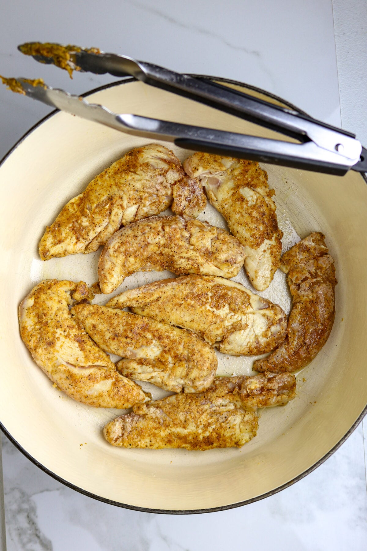 A pot of browned chicken tenders with tongs resting on the edge for Marry Me Chicken.