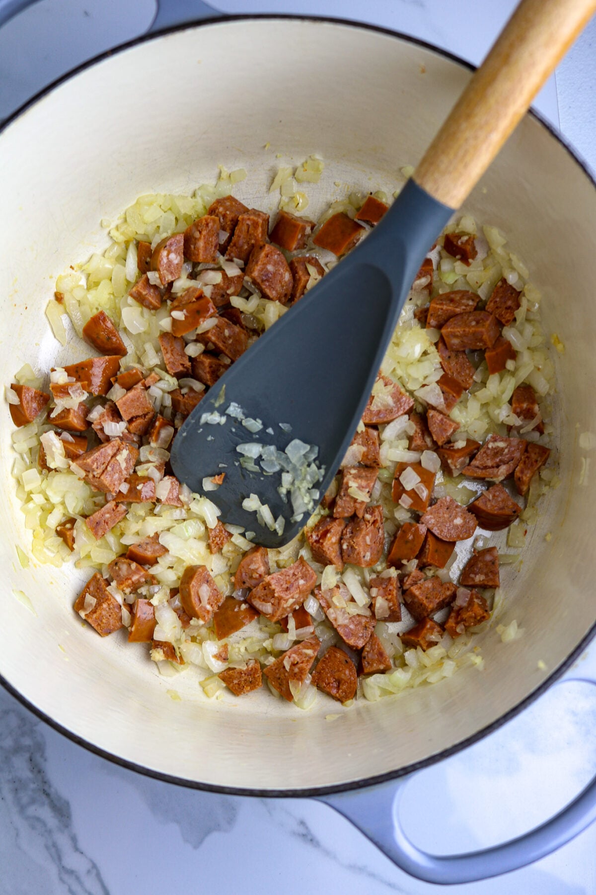 A spoon stirring a pot of chopped sausage in chopped onion.