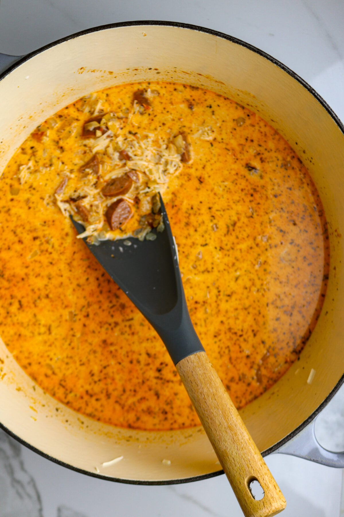 A spoon stirring a golden creamy mixture with sausage and cheese.
