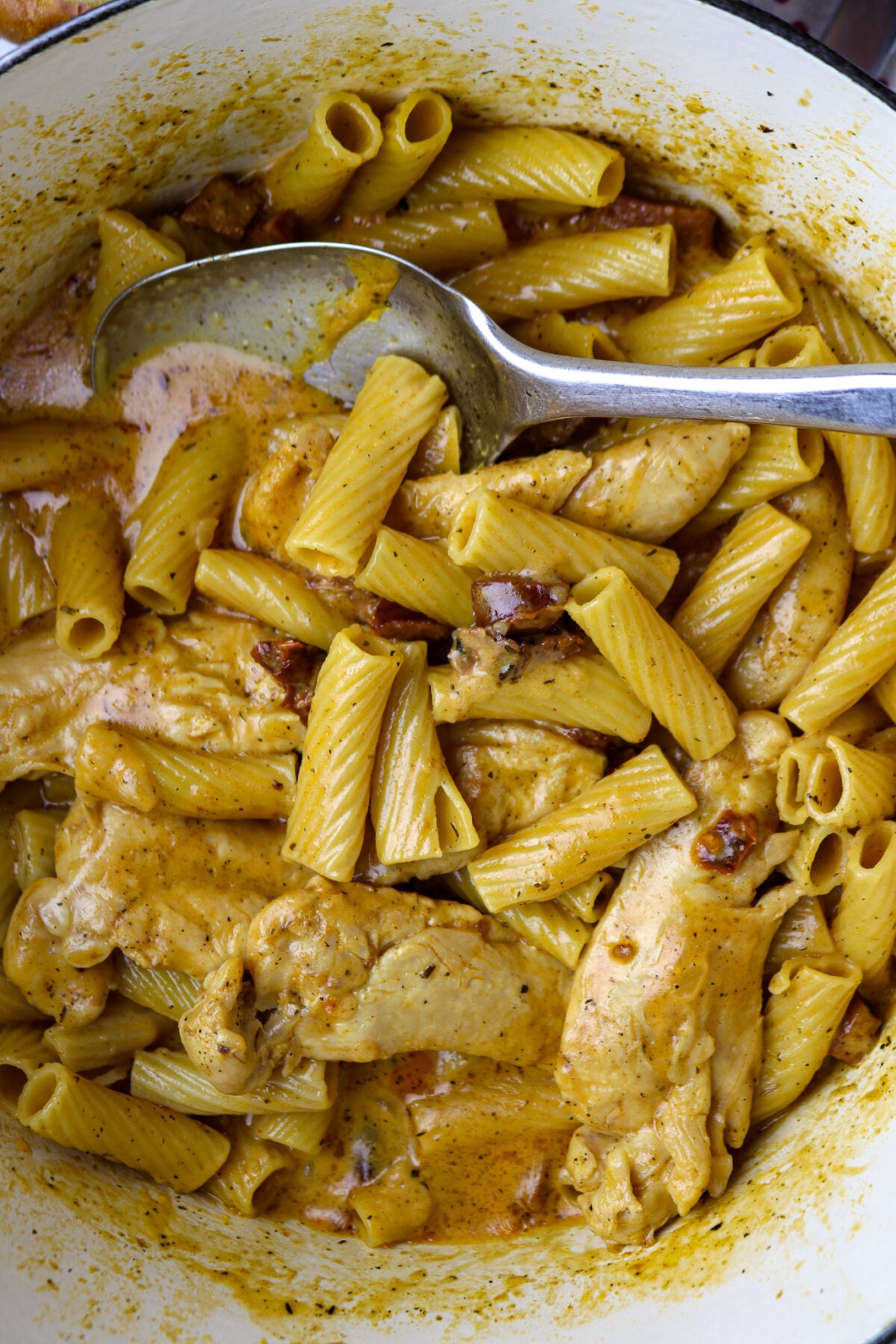 A close up of pasta and sauce with chicken for marry me chicken with a silver spoon in it.