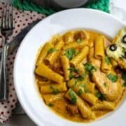 A white pasta bowl of chicken, pasta, sausage, in a luscious sauce sprinkled with chopped parsley.