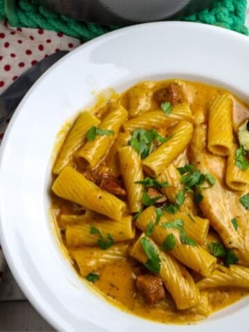 A white pasta bowl of chicken, pasta, sausage, in a luscious sauce sprinkled with chopped parsley.