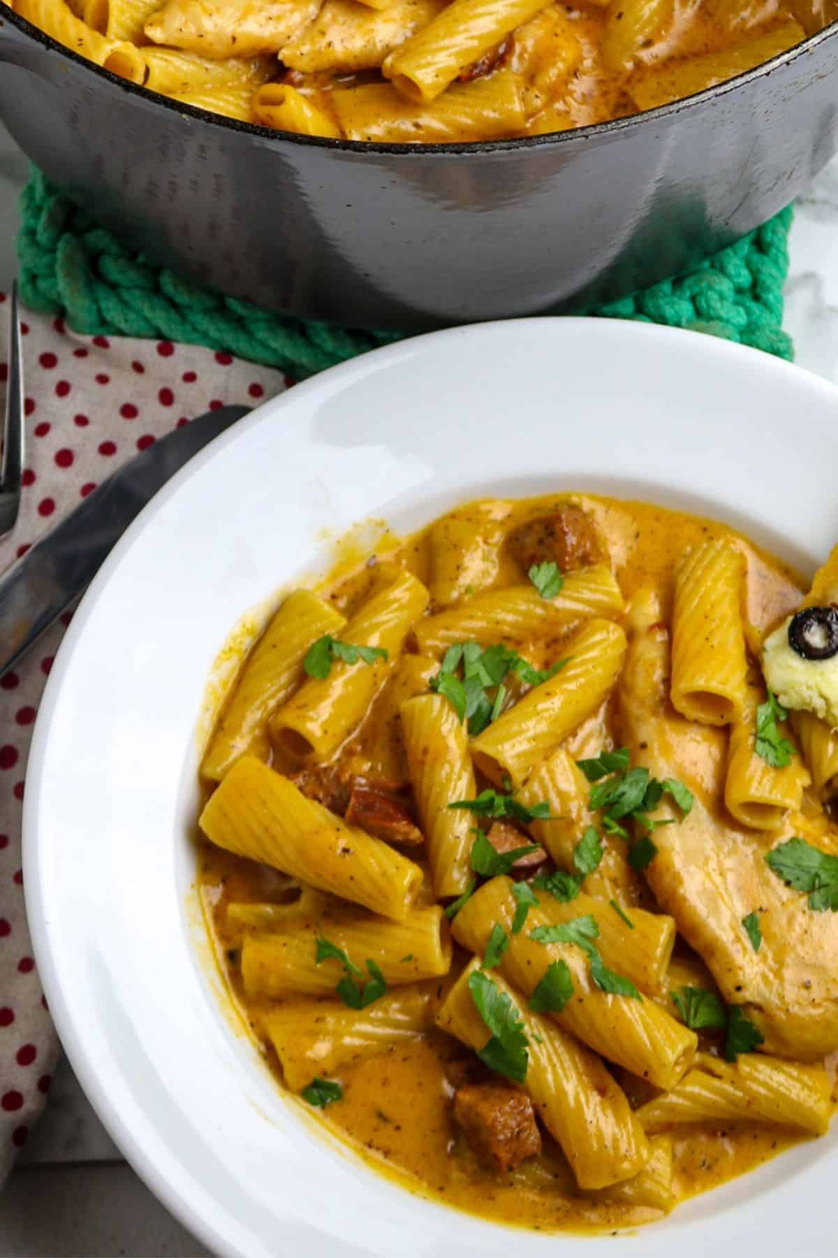 A white pasta bowl of chicken, pasta, sausage, in a luscious sauce sprinkled with chopped parsley.