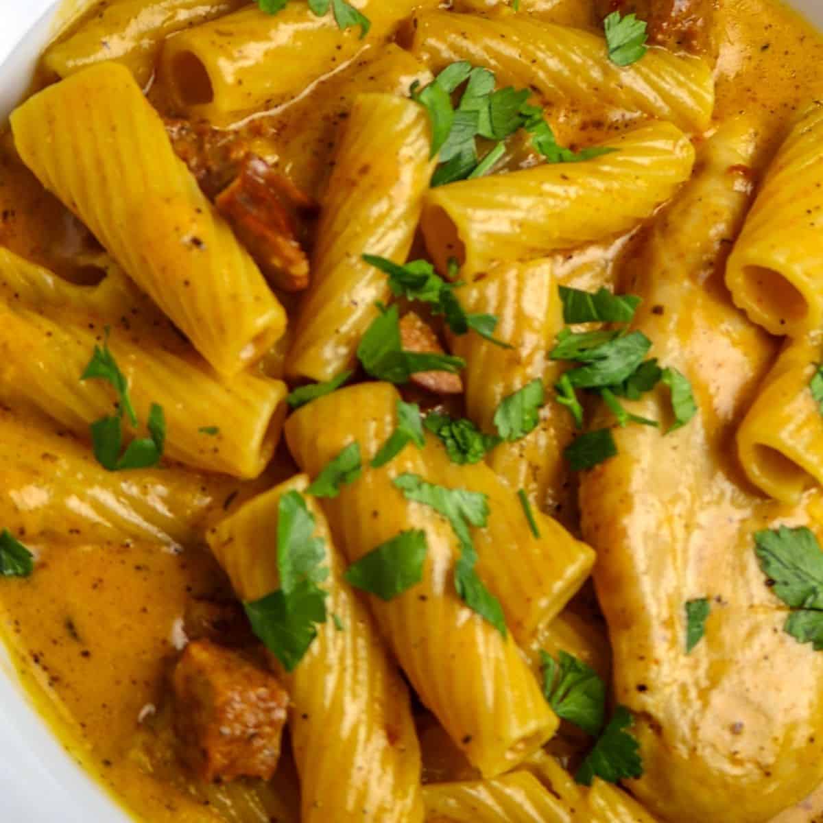 A closeup of a luscious bowl of rigatoni pasta, chicken, sausage, and sprinkled with parsley.