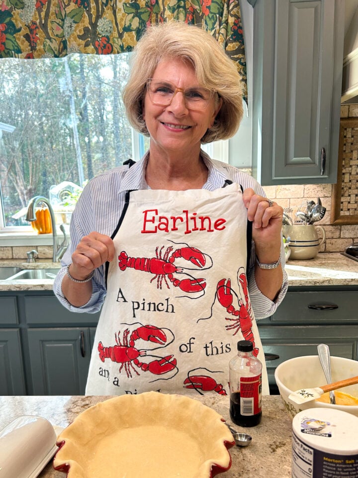 Photo of Kay wearing her mother's apron with Earline written across it in her kitchen making pies.