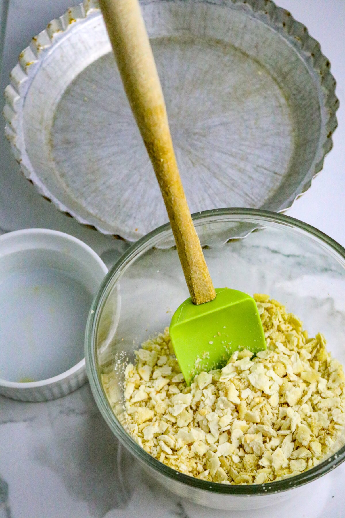 A glass bowl of crushed crackers and a green spoonula in it.