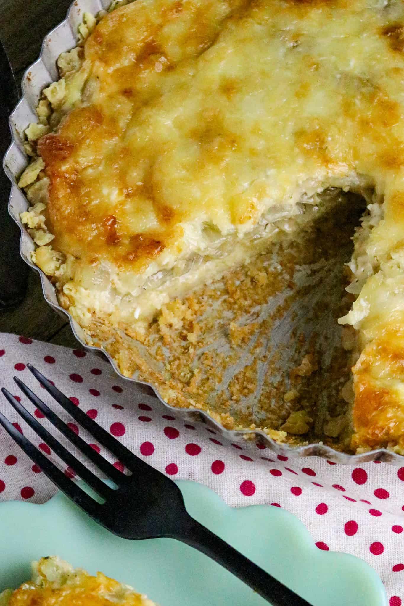 A cheese topped onion pie with a piece cut out of it.