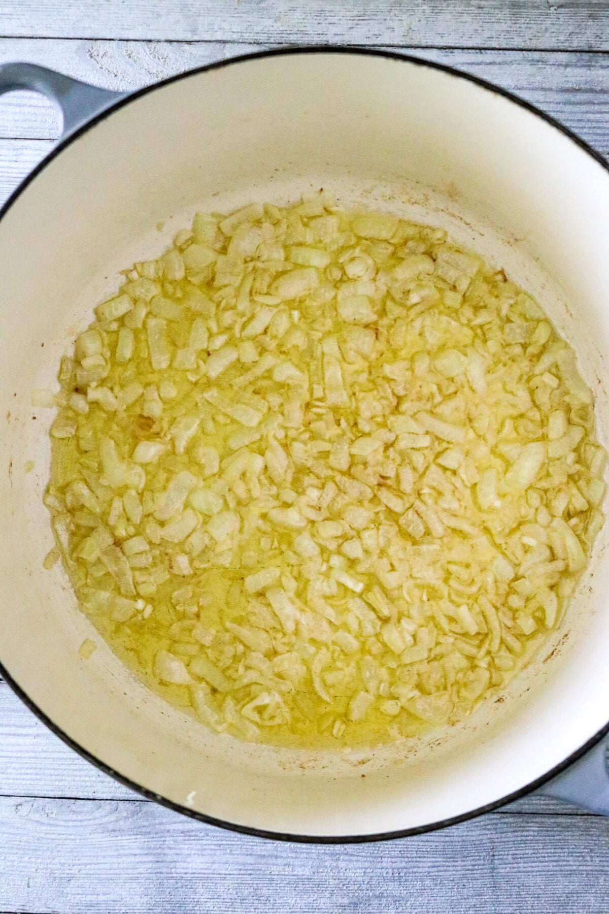 A Dutch oven pot with chopped onions cooked in butter.