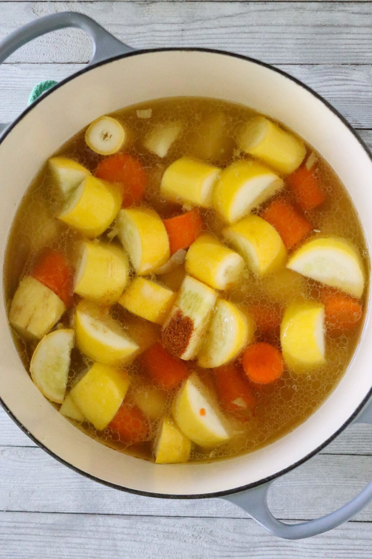 A Dutch oven pot with chunks of carrots, potatoes, and squash in chicken broth with seasonings in it.