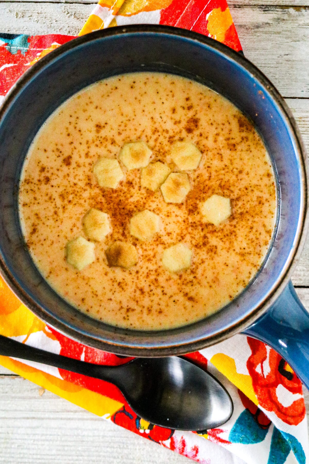 A blue bowl with squash bisque and oyster crackers on top with a black spoon and a colorful napkin next to it.