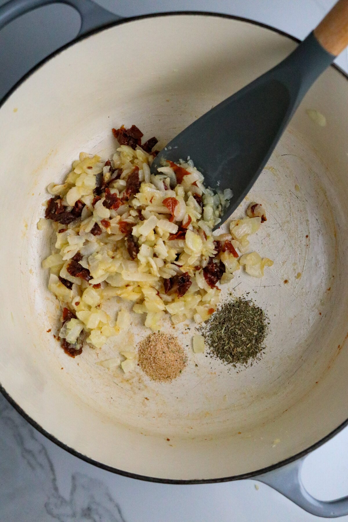 A dark long-handled spoon stirring chopped vegetables with seasonings in a large Dutch oven pot.