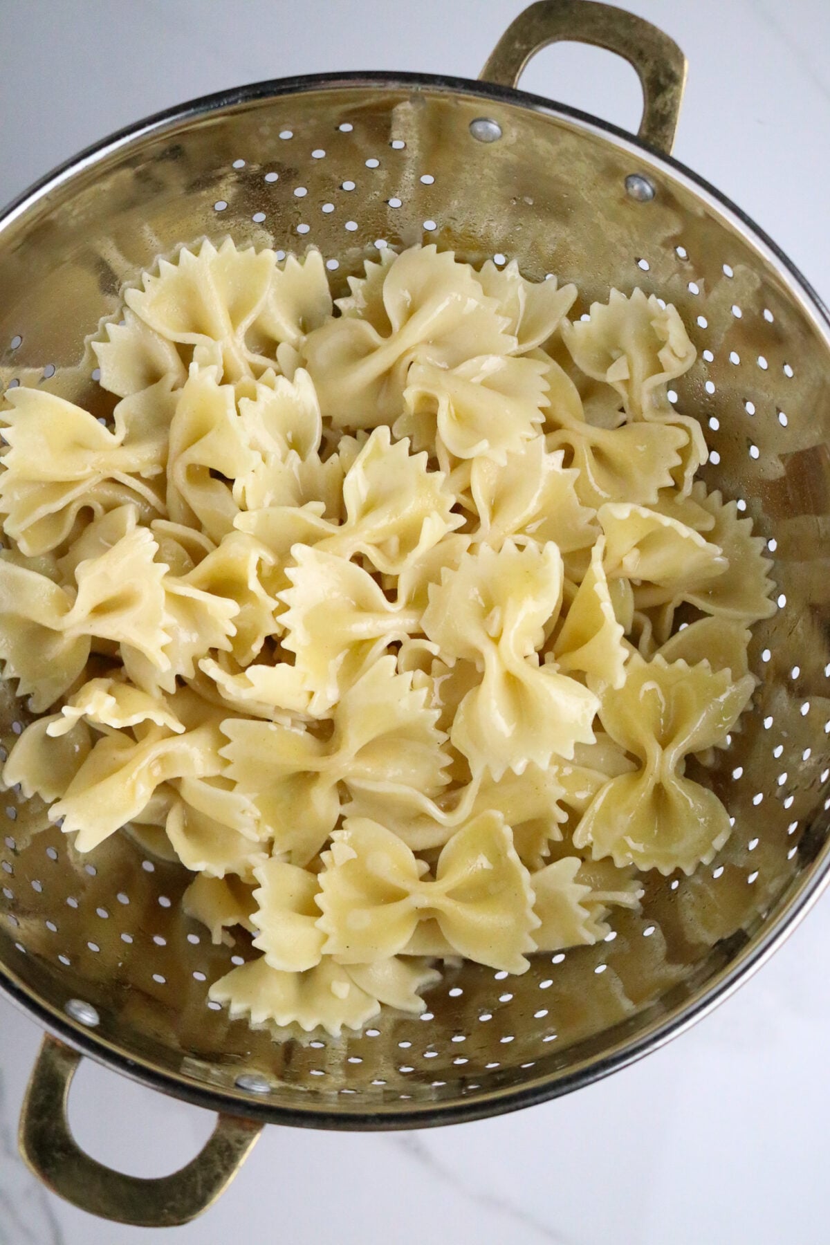 A metal strainer with cooked bowtie pasta.