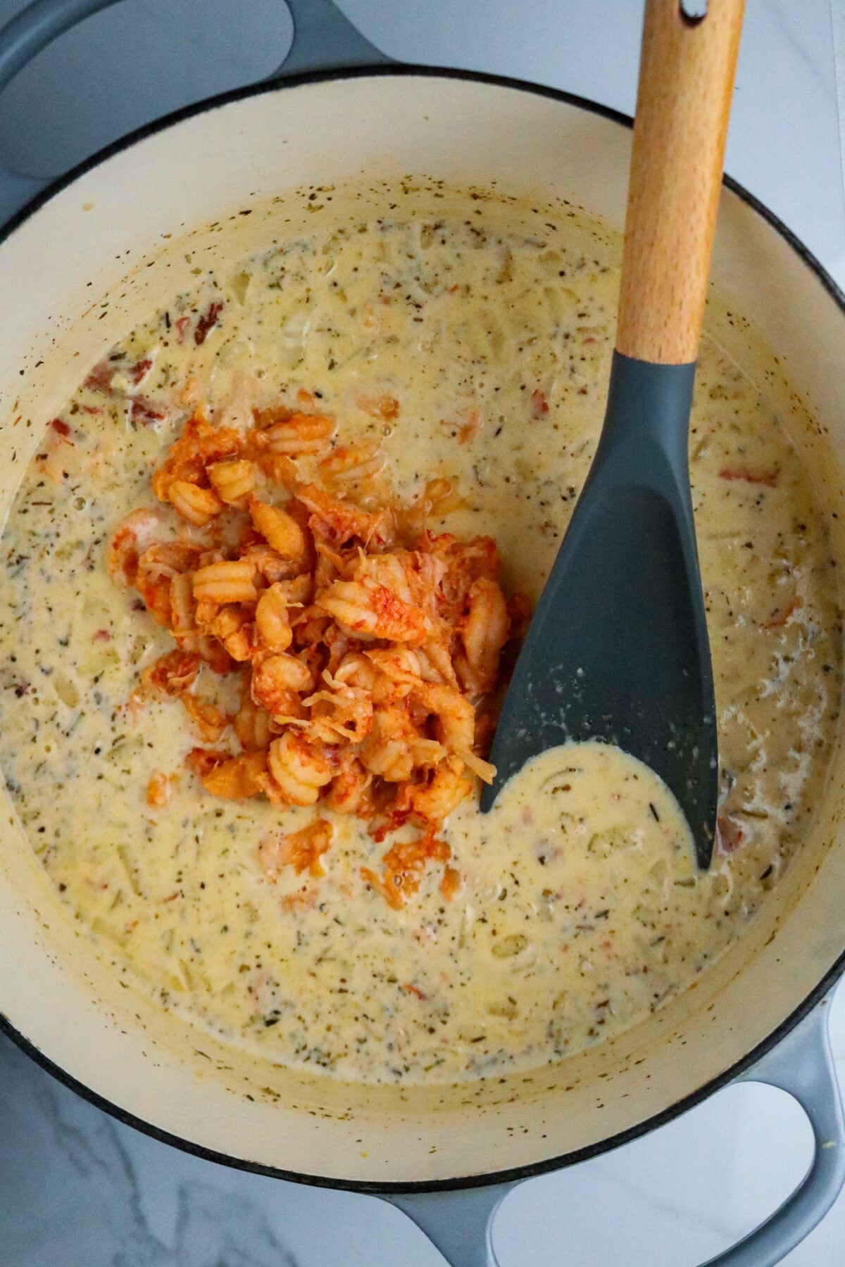 A Dutch oven pot with a spoon stirring crawfish tails into a cheesy cream sauce.