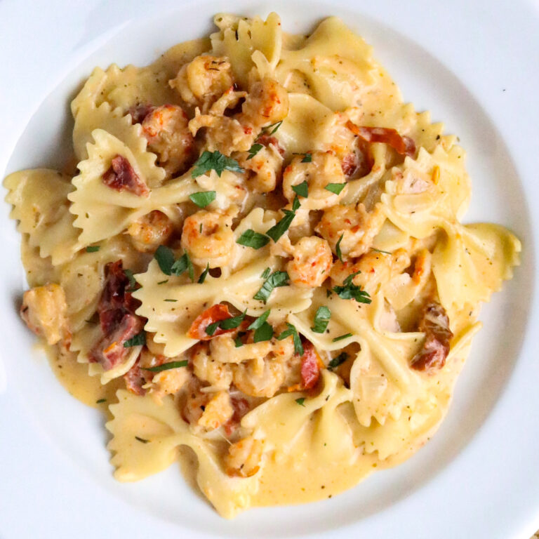 A serving of Marry Me Crawfish which is bowtie pasta in a cream sauce with crawfish in a white pasta bowl.