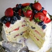 A white 3 layer cake with vanilla frosting and fresh berries on top.