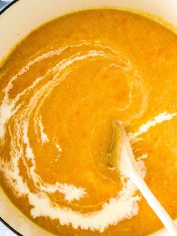 A Dutch oven pot with a squash soup and wooden spoon stirring cream into the soup.