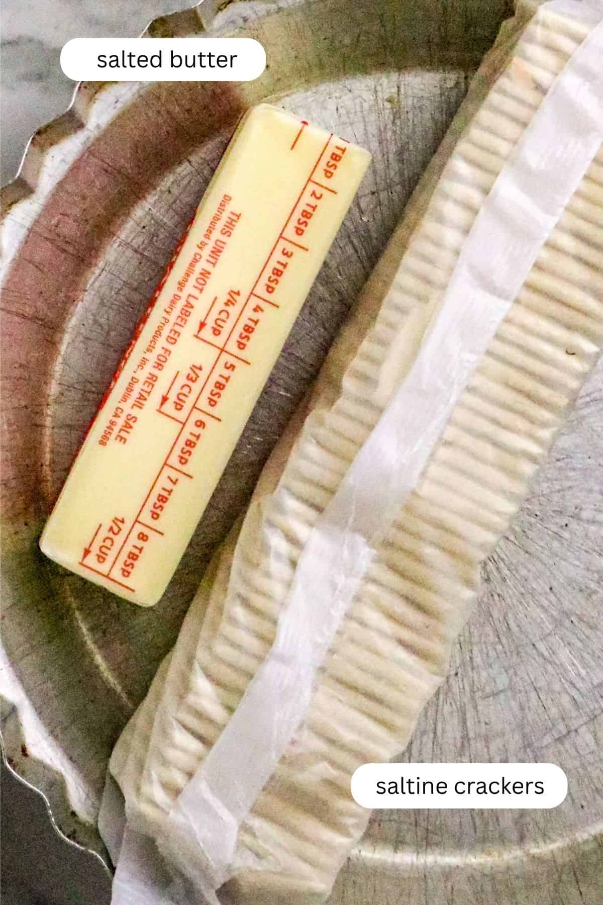 A stick of butter and a pack of saltine crackers in a metal pie pan.