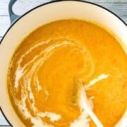 A Pinterest Pin with a Dutch oven pot with a yellow squash bisque and wooden spoon stirring cream into the soup.