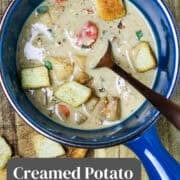 A blue bowl of creamed potato and carrot soup with a spoon in it.