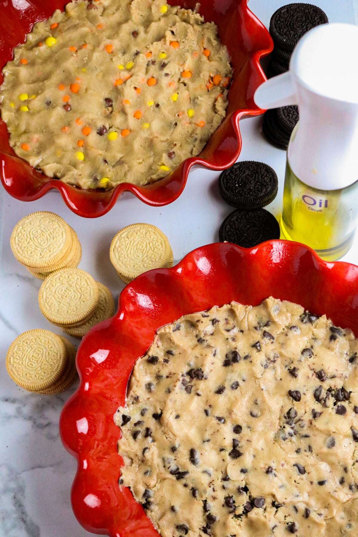 Two red pie pans with vanilla and chocolate Oreos scattered around and a spray oil container.