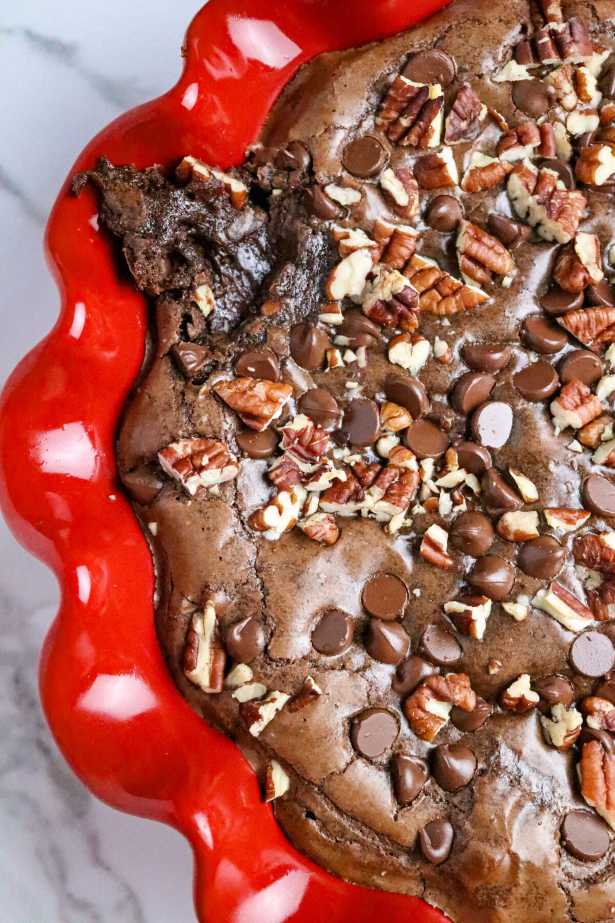 A chocolate pie with a brownie crust and chocolate chips with chopped pecans on top in a red pie pan.