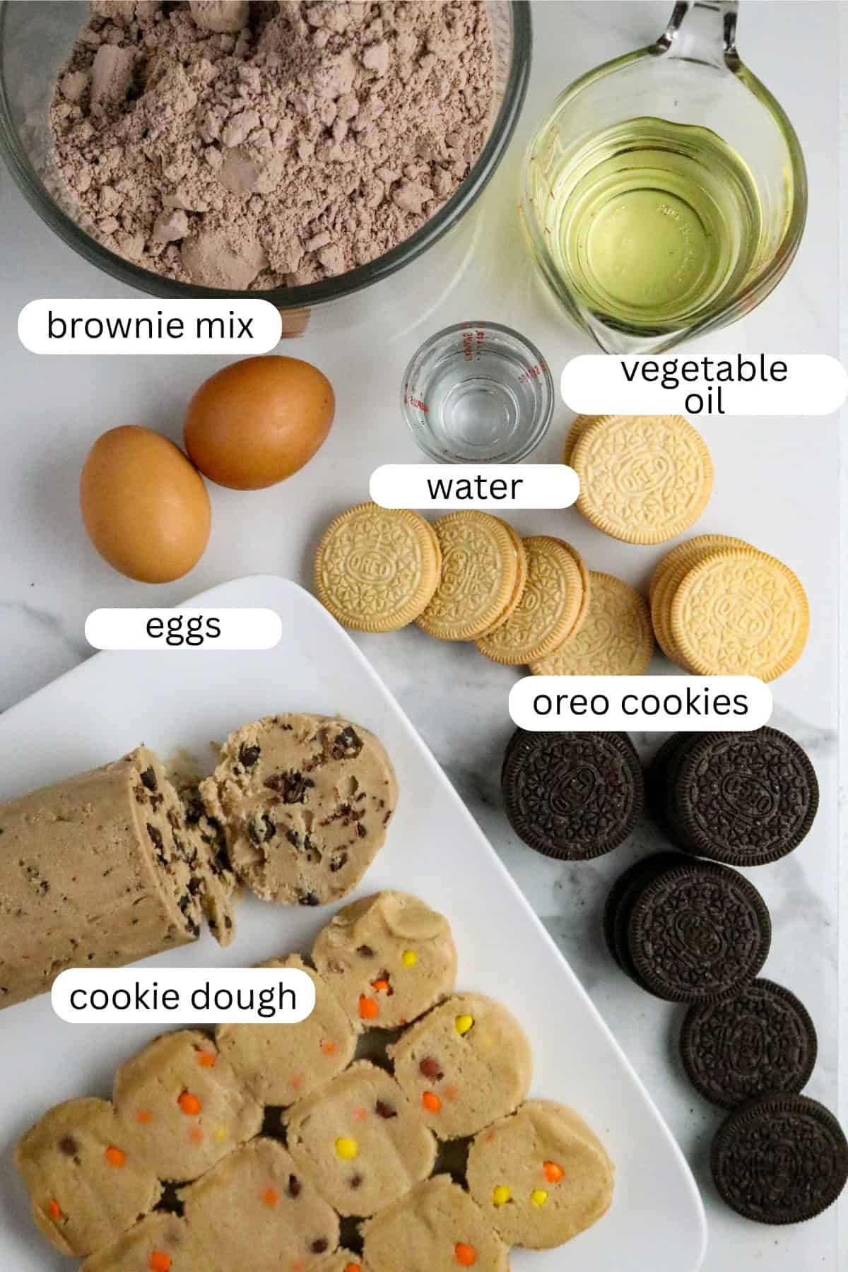 Ingredients of cookie dough, sandwich cookies, eggs brownie mix, and oil on a white countertop.